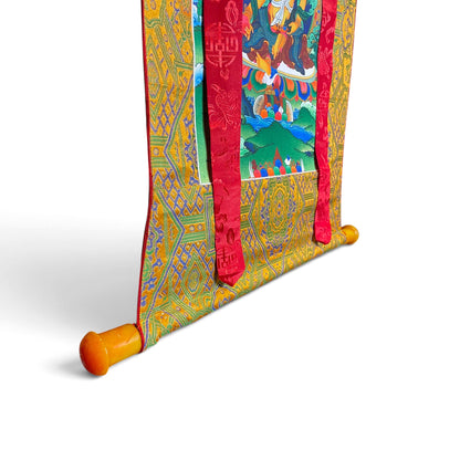Thangka Dzambhala, détail de la barre aux extrémités orange et du brocart – Himalaya Vibes