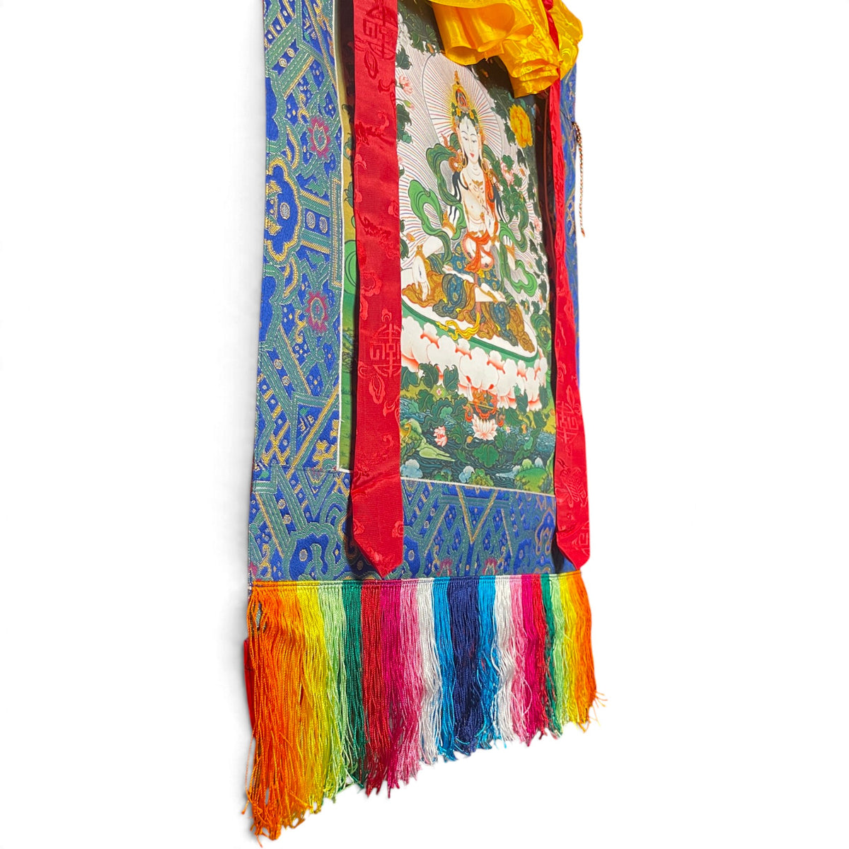 Frange colorate e cornice in broccato blu in basso sul thangka Tara bianca