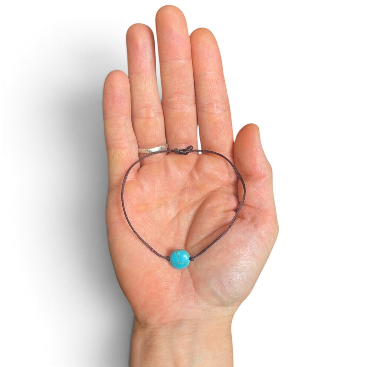 Bracelet brun avec perle bleu turquoise dans la paume pour montrer la taille