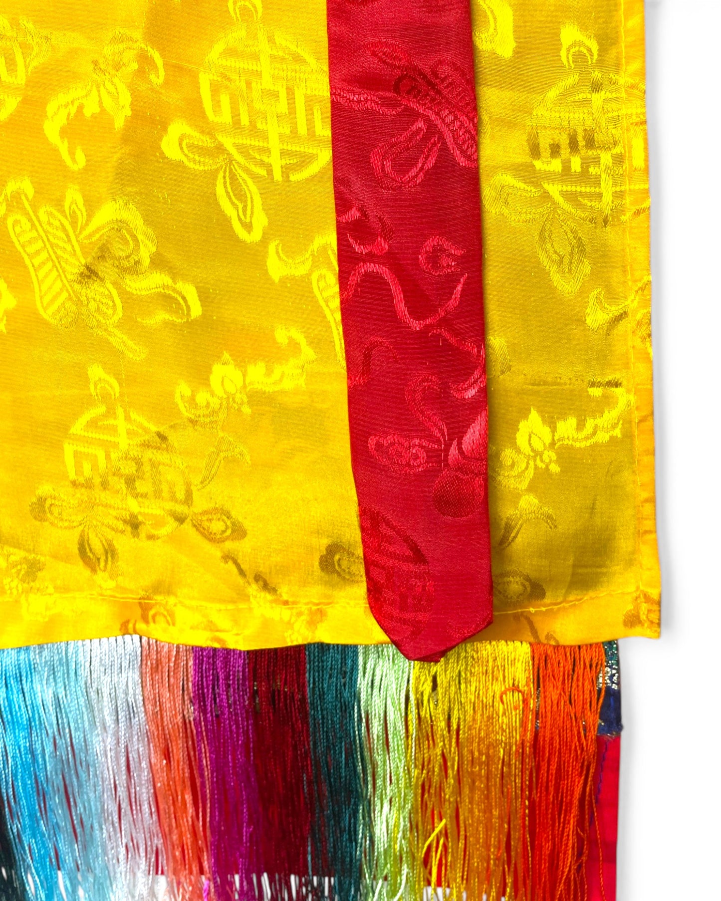 Detailansicht der gelben Seide und der roten Baender des Thangka-Schutzvorhangs.
