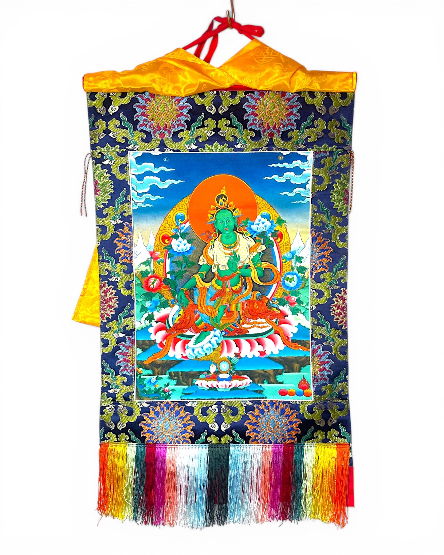 Gesamtansicht des Gruene Tara Thangkas mit blauem Brokatrahmen und bunten Fransen.