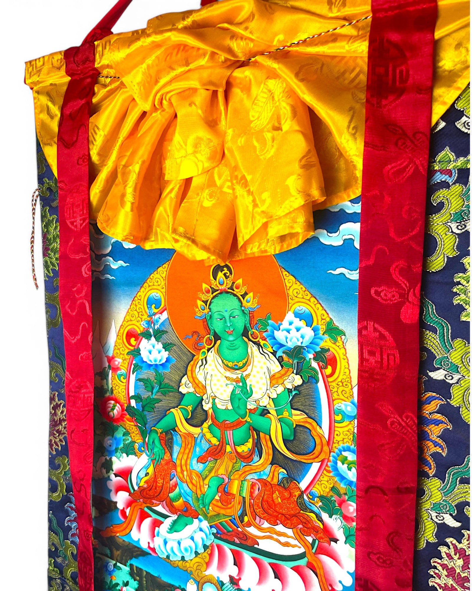 Seitenansicht des Gruene Tara Thangkas mit kunstvoll drapiertem gelben Schutzvorhang und roten Baendern.