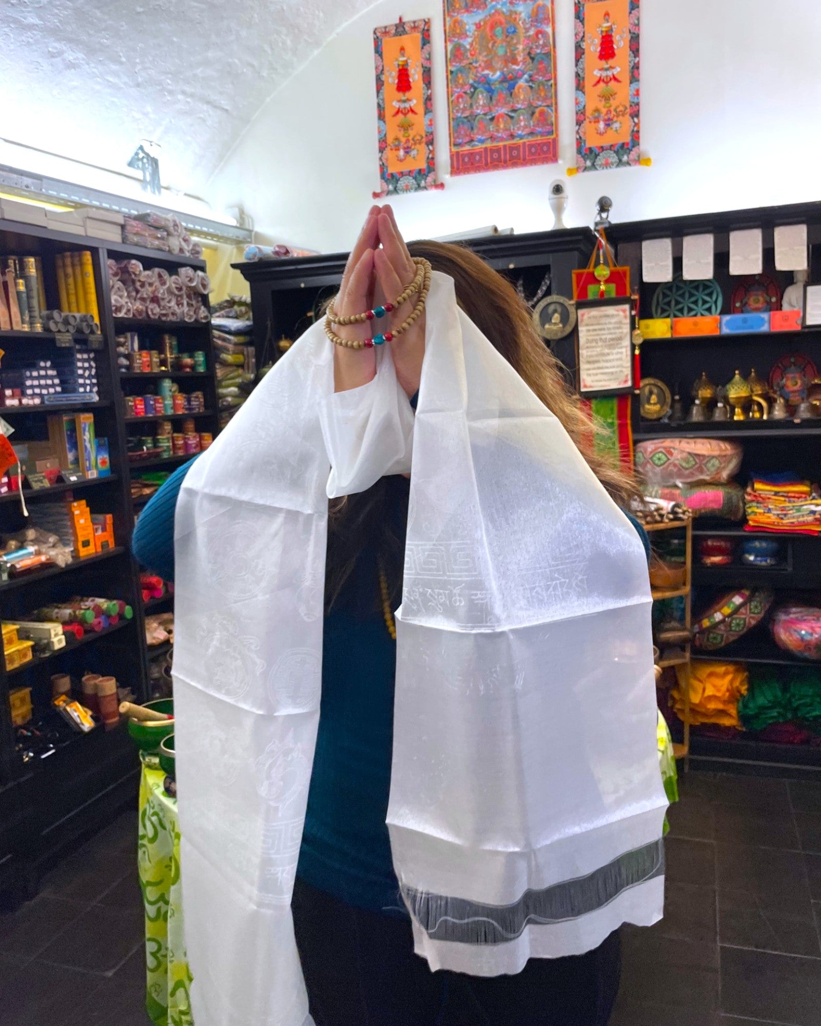 Respektvolle Geste: Frau hält den Khata Schal mit gefalteten Händen vor das Gesicht, Mala Perlen sichtbar.