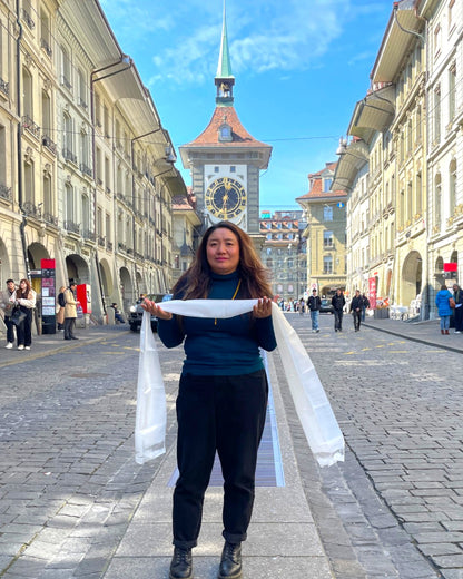 Eine Frau präsentiert einen weißen Khata Zeremonialschal vor der Zytglogge in der Berner Altstadt.