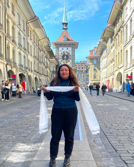 Eine Frau präsentiert einen weißen Khata Zeremonialschal vor der Zytglogge in der Berner Altstadt.