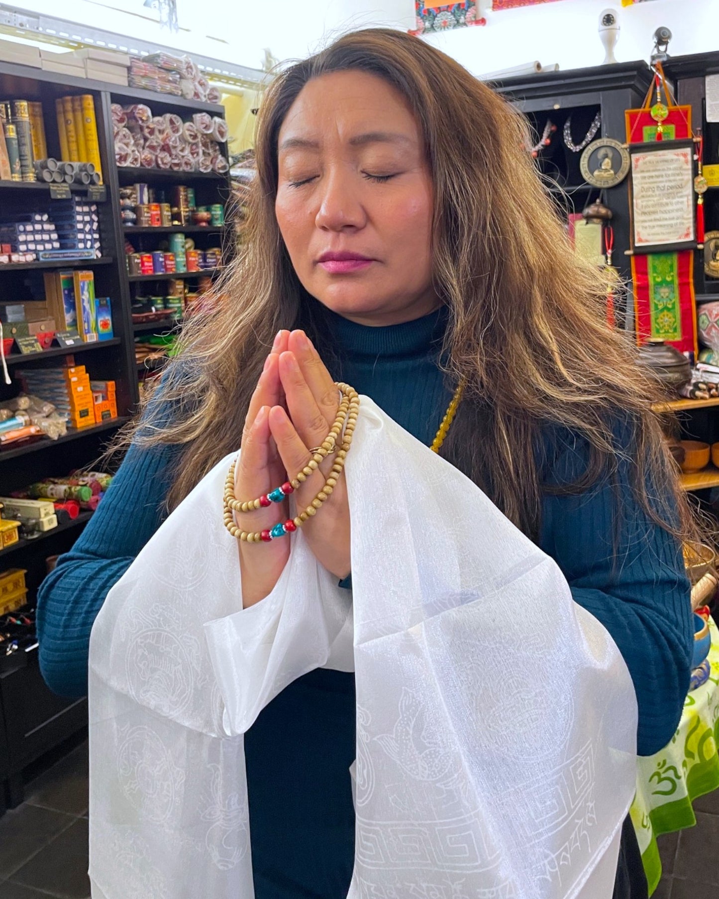 Eine Frau meditiert mit geschlossenen Augen, hält einen Khata Schal und eine Mala Gebetskette.