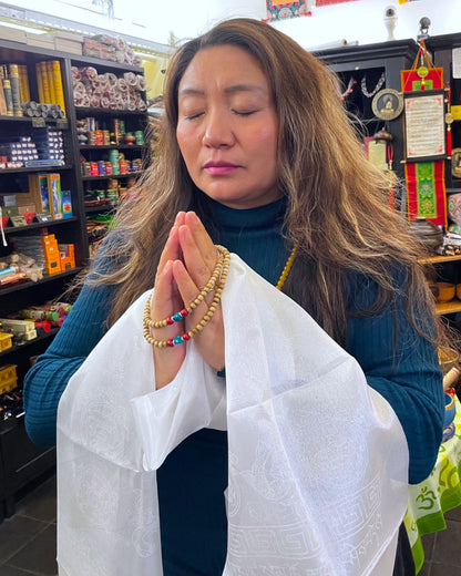 Eine Frau meditiert mit geschlossenen Augen, hält einen Khata Schal und eine Mala Gebetskette.