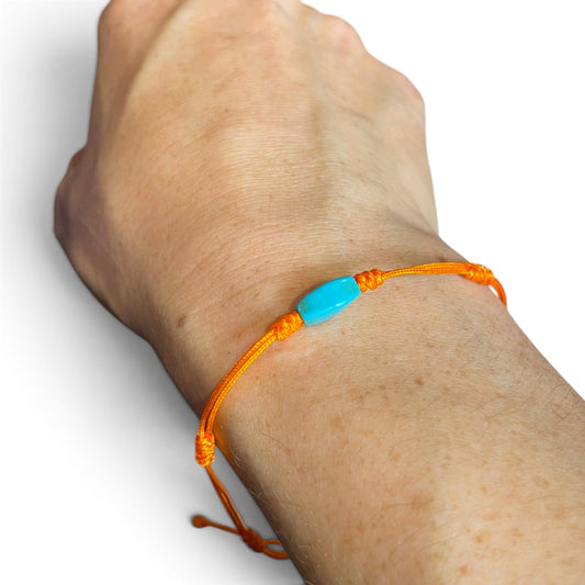 Orangefarbenes Knoten-Armband mit türkisblauer Perle am Handgelenk getragen