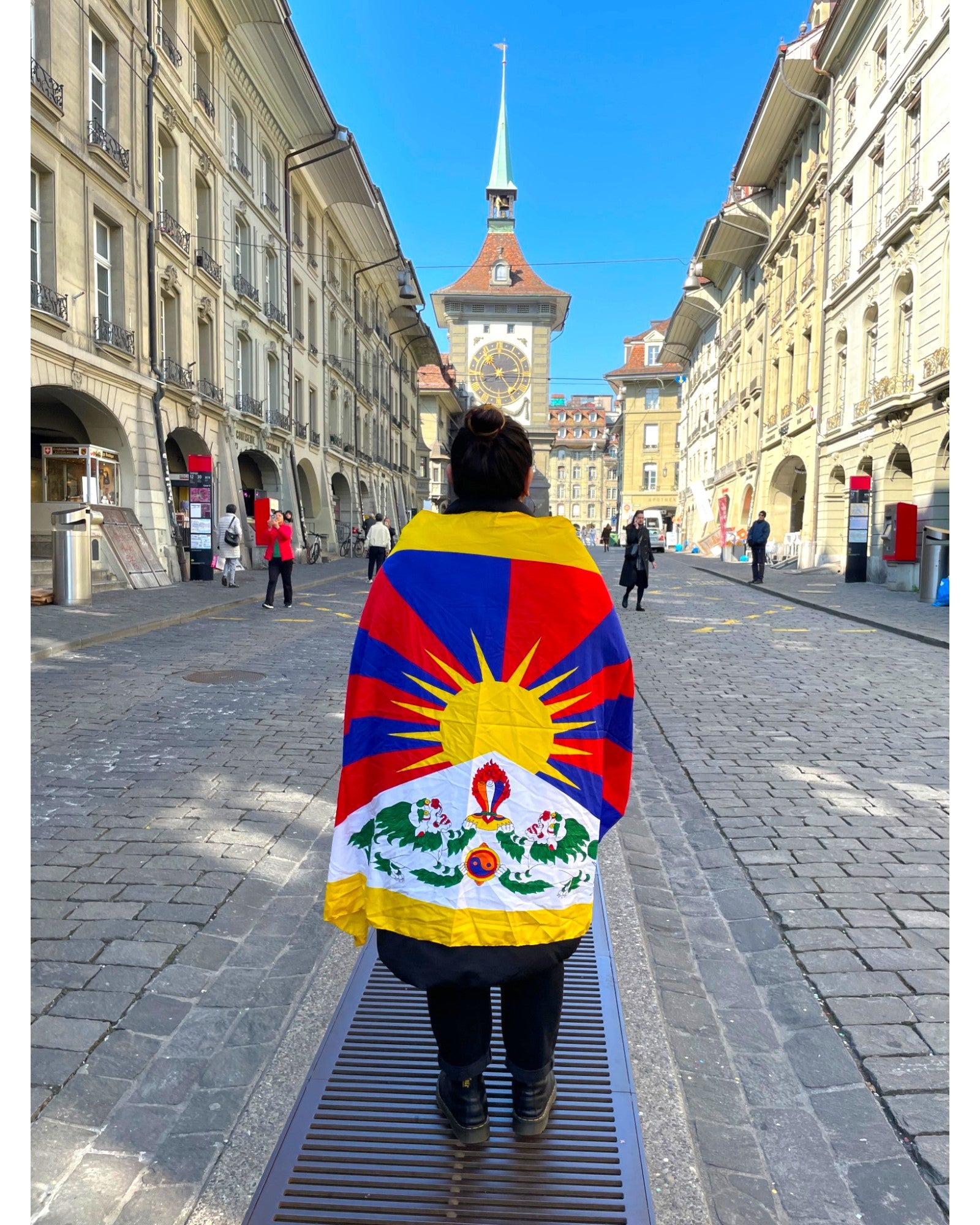 Rueckansicht einer Person mit der Tibet Nationalflagge in den Gassen von Bern