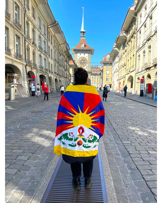 Rueckansicht einer Person mit der Tibet Nationalflagge in den Gassen von Bern